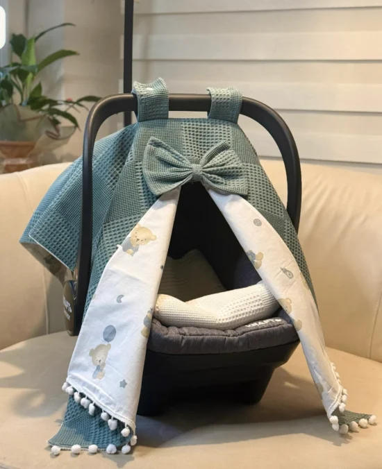 Waffle cotton baby car seat canopy with printed poplin lining, bow detail, and pom pom trim on an infant car seat.
