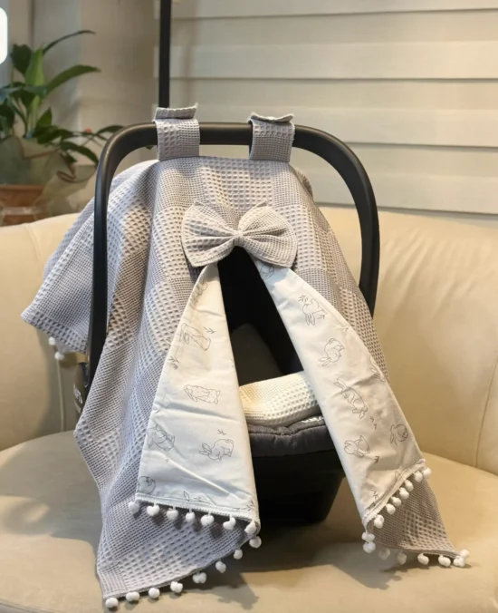 Waffle cotton baby car seat canopy with printed poplin lining, bow detail, and pom pom trim on an infant car seat.