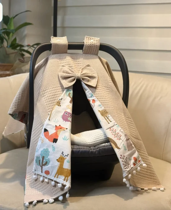 Waffle cotton baby car seat canopy with printed poplin lining, bow detail, and pom pom trim on an infant car seat.