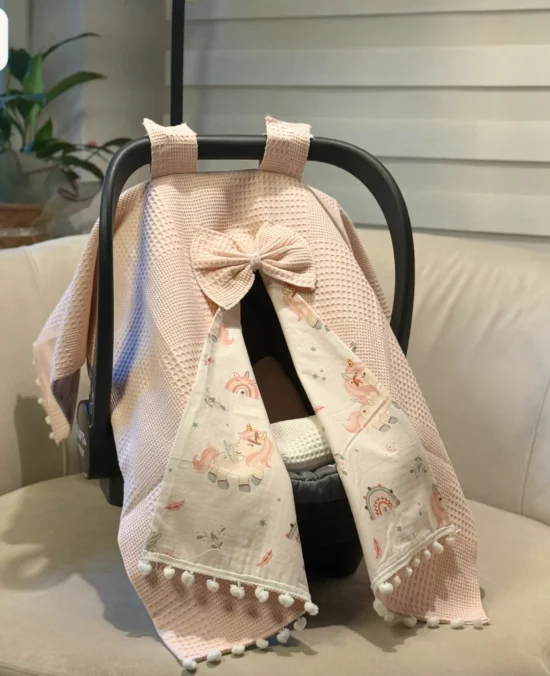 Waffle cotton baby car seat canopy with printed poplin lining, bow detail, and pom pom trim on an infant car seat.
