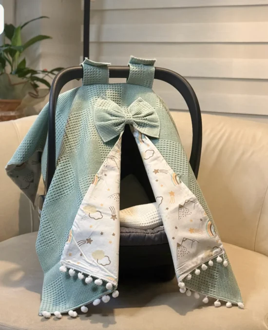 Waffle cotton baby car seat canopy with printed poplin lining, bow detail, and pom pom trim on an infant car seat. Patina Blue