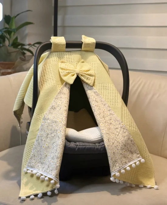 Waffle cotton baby car seat canopy with printed poplin lining, bow detail, and pom pom trim on an infant car seat.