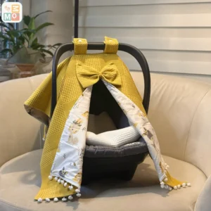 Waffle cotton baby car seat canopy with printed poplin lining, bow detail, and pom pom trim on an infant car seat.cotton baby car seat cover