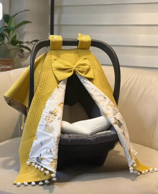 Waffle cotton baby car seat canopy with printed poplin lining, bow detail, and pom pom trim on an infant car seat.cotton baby car seat cover
